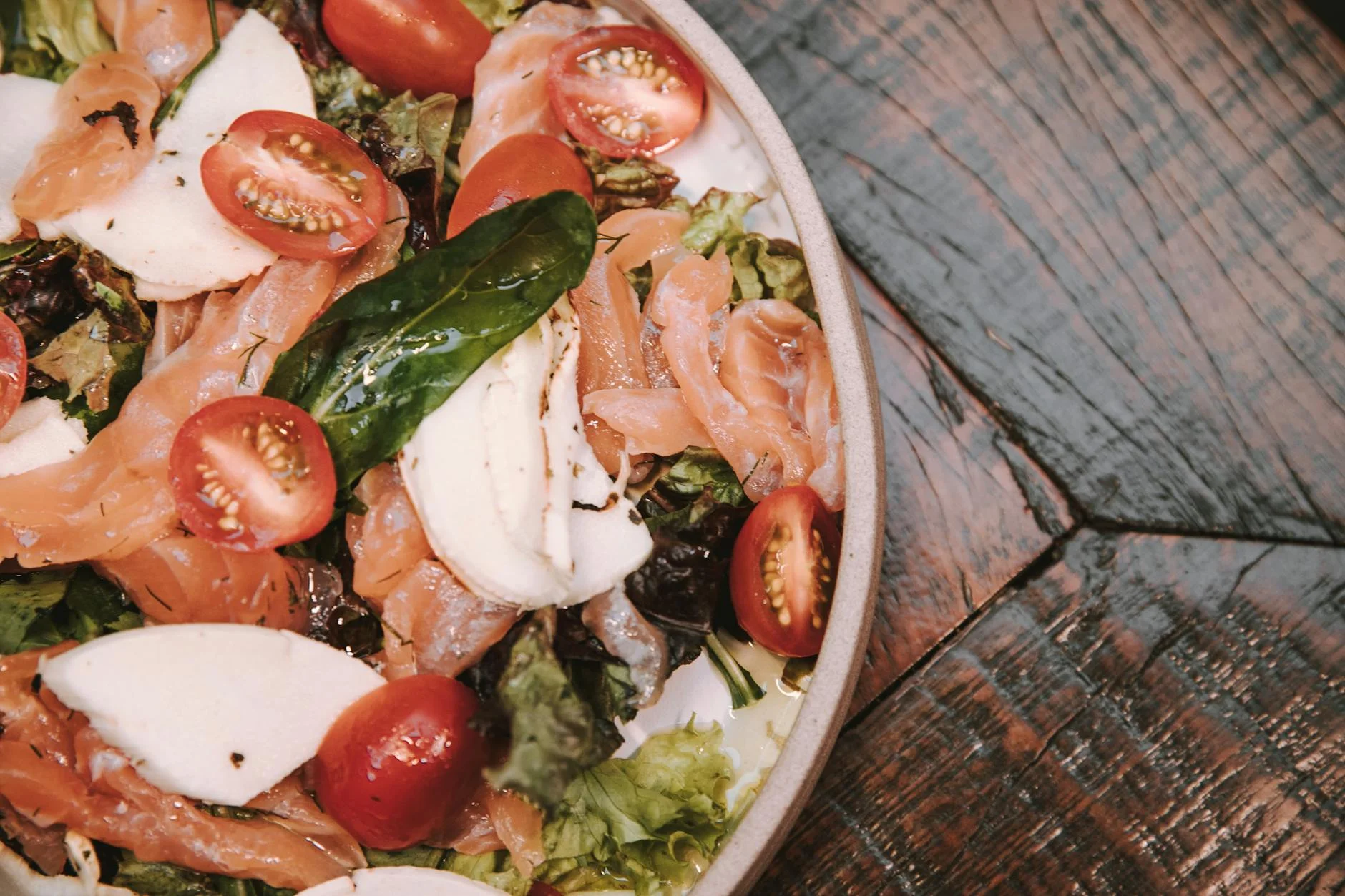 A vibrant fresh salad with smoked salmon, mozzarella, and cherry tomatoes on a rustic table. — Foto: Victor Miyata / Pexels