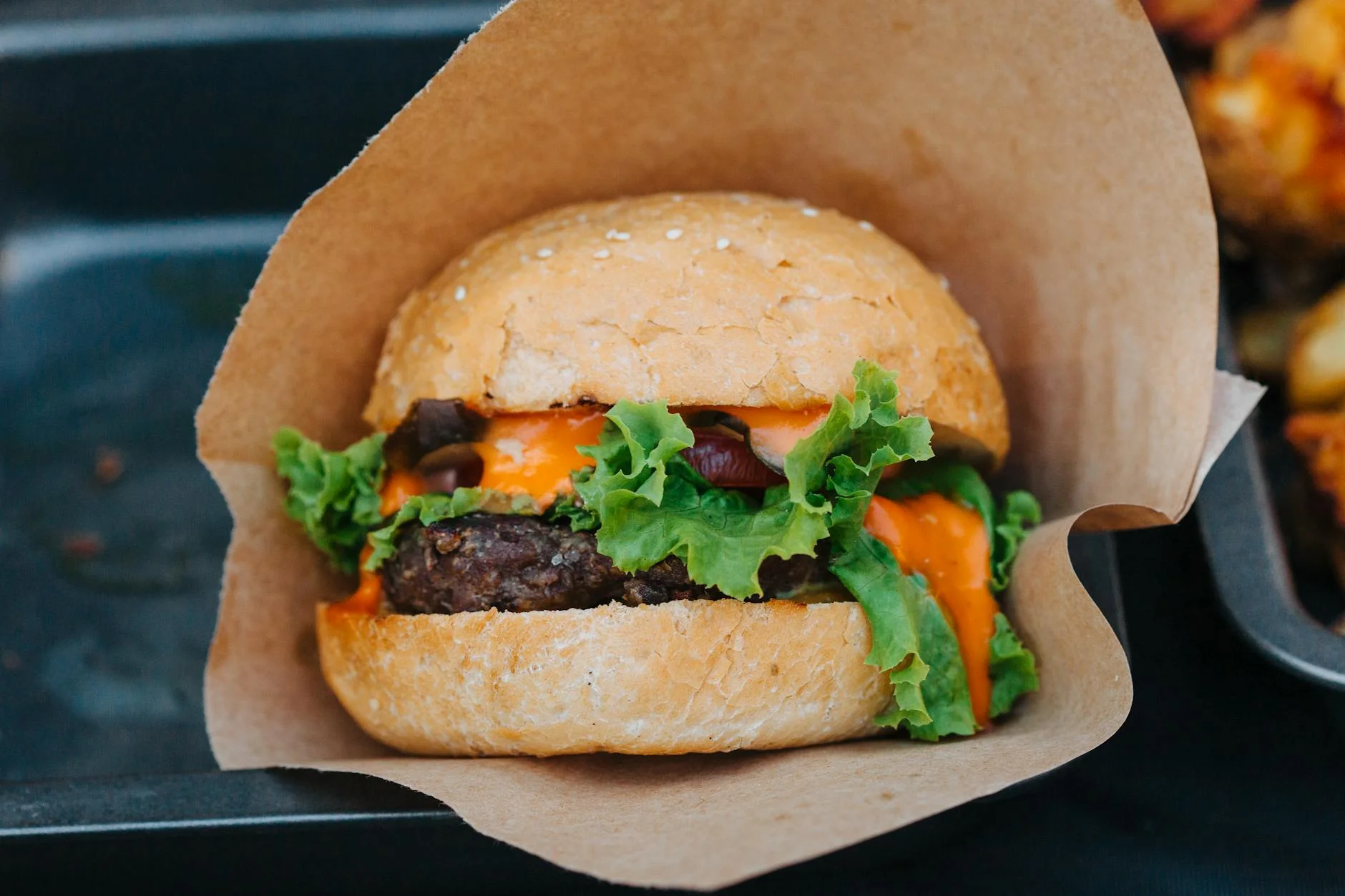 A vibrant, photorealistic vegetarian plate showcasing diverse plant-based 'meat' alternatives: crispy pan-fried tofu cubes, savory mushroom 'steaks', and shredded jackfruit 'pulled pork' on a bun, all artfully arranged. Cinematic lighting, sharp focus on the textures and details, depth of field, 8K, professional photography, shot on a high-end DSLR. Close-up of a delicious cheeseburger with fresh lettuce and creamy sauce wrapped in paper. — Foto: Julia Filirovska / Pexels
