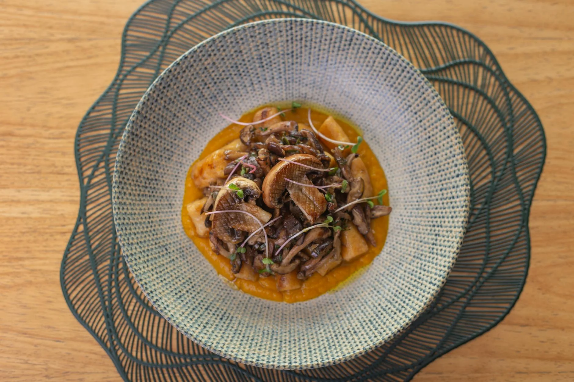 A photorealistic, professional photography shot of a deconstructed gourmet vegetarian soup, showcasing various textural elements: a creamy base in a bowl, with small piles of crispy roasted chickpeas, toasted pumpkin seeds, fresh herb sprigs, and delicate vegetable crisps arranged around it. Cinematic lighting emphasizes the contrast in textures and colors. Sharp focus on the food, with a soft depth of field. 8K hyper-detailed, shot on a high-end DSLR. Delicious gourmet mushroom dish served in a textured bowl on a wooden table. — Foto: Fernanda da Silva Lopes / Pexels