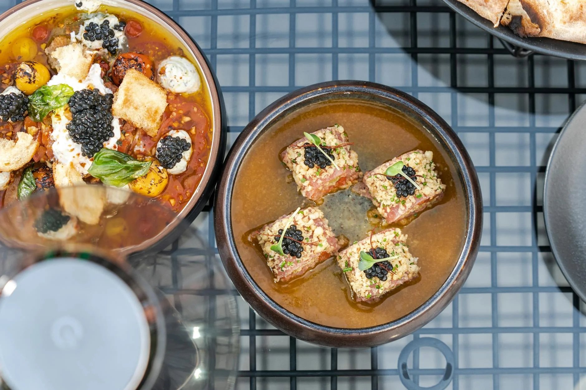 A photorealistic, professional photography shot of a perfectly plated bowl of gourmet vegetarian soup, with a delicate swirl of cashew cream, a sprinkle of fresh chopped chives, and a few crispy roasted chickpeas on top. The soup is in a rustic, elegant ceramic bowl on a dark wooden table, illuminated by soft, cinematic lighting. The focus is sharp on the garnishes, highlighting their intricate details and vibrant colors. 8K hyper-detailed, shot on a high-end DSLR. Overhead view of elegant caviar dishes in stylish bowls, showcasing modern dining aesthetics. — Foto: Denys Gromov / Pexels
