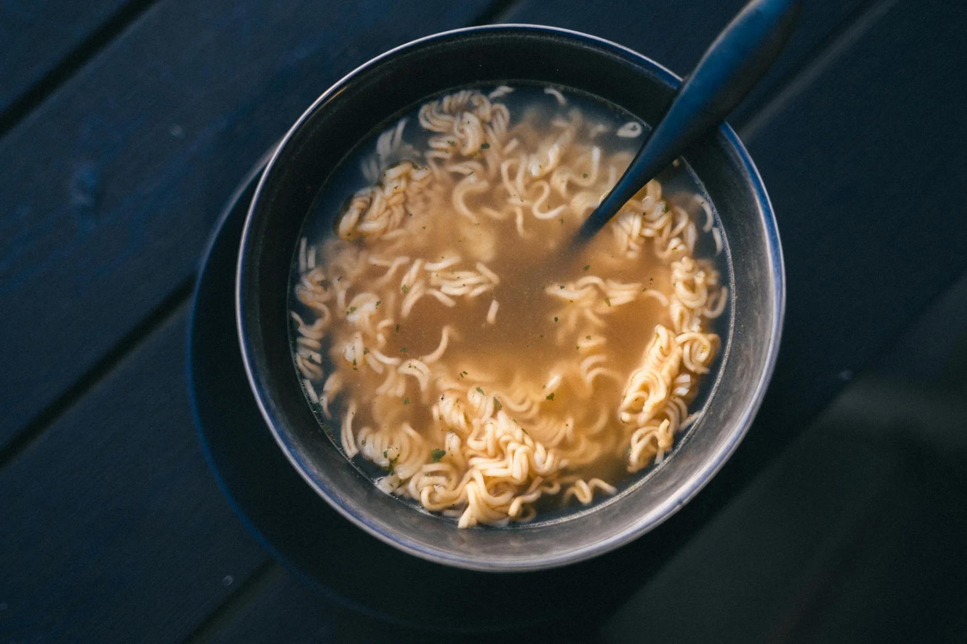 A photorealistic, professional photography shot of a large pot of ramen broth gently simmering on a stovetop, with delicate steam rising. The broth is a rich, clear amber color, indicating careful simmering. Cinematic lighting highlights the surface, sharp focus, depth of field, 8K, shot on a high-end DSLR. A close-up view of a warm bowl of instant ramen noodles with broth on a dark surface. — Foto: Diana ✨ / Pexels