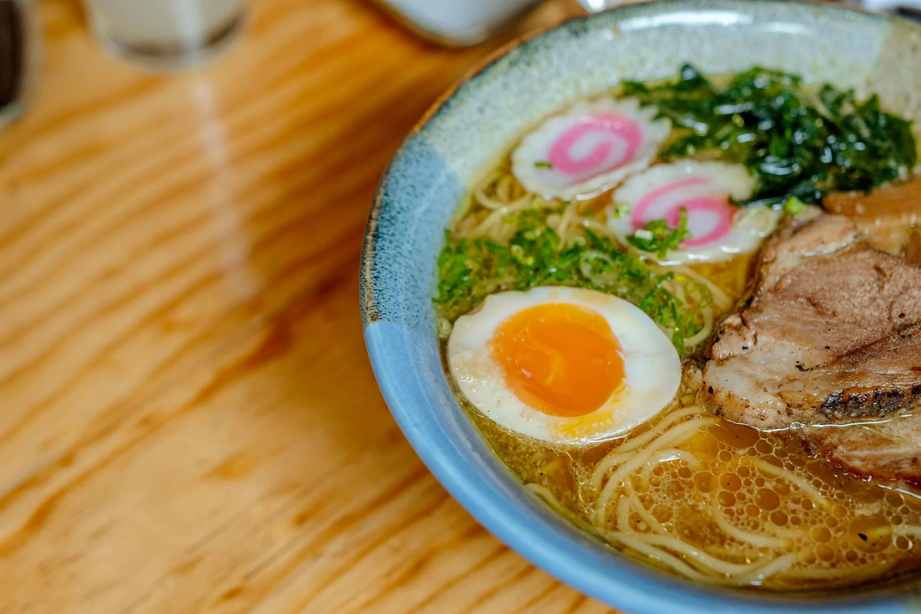 A photorealistic, professional photography image of a chef's hands carefully tasting a spoonful of ramen broth from a simmering pot, with a thoughtful, concentrated expression. The kitchen background is slightly blurred, emphasizing the act of tasting and refinement. 8K, cinematic lighting, sharp focus, depth of field, shot on a high-end DSLR. Close-up of a savory Japanese ramen bowl featuring noodles, egg, and toppings on a wooden table. — Foto: Viridiana Rivera / Pexels