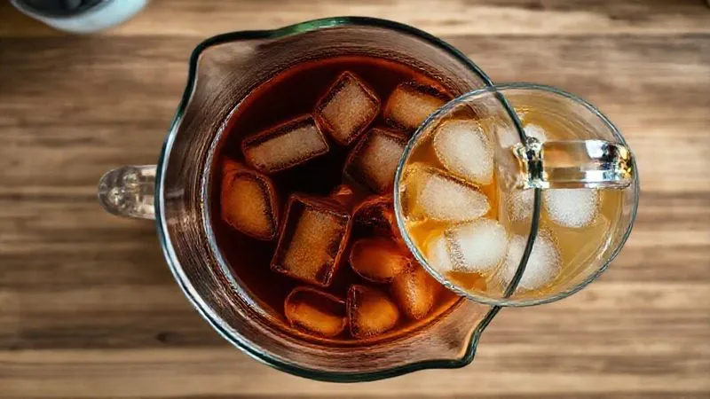 A photorealistic, top-down view of two transparent glass pitchers. One pitcher contains a dark, rich, concentrated iced tea, while the other holds a lighter, more diluted version. The contrast in color and perceived density is clear. Cinematic lighting, sharp focus on the liquids, depth of field blurring a kitchen counter. 8K hyper-detailed, professional photography, shot on a high-end DSLR. Illustrates the concept of concentration.