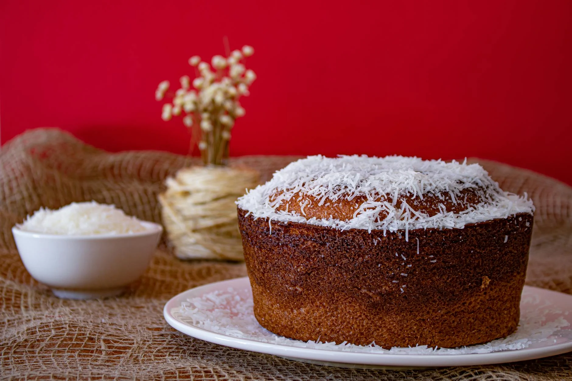A mouthwatering homemade coconut cake with shredded coconut topping against a vibrant red backdrop. — Foto: Bruno Curly / Pexels