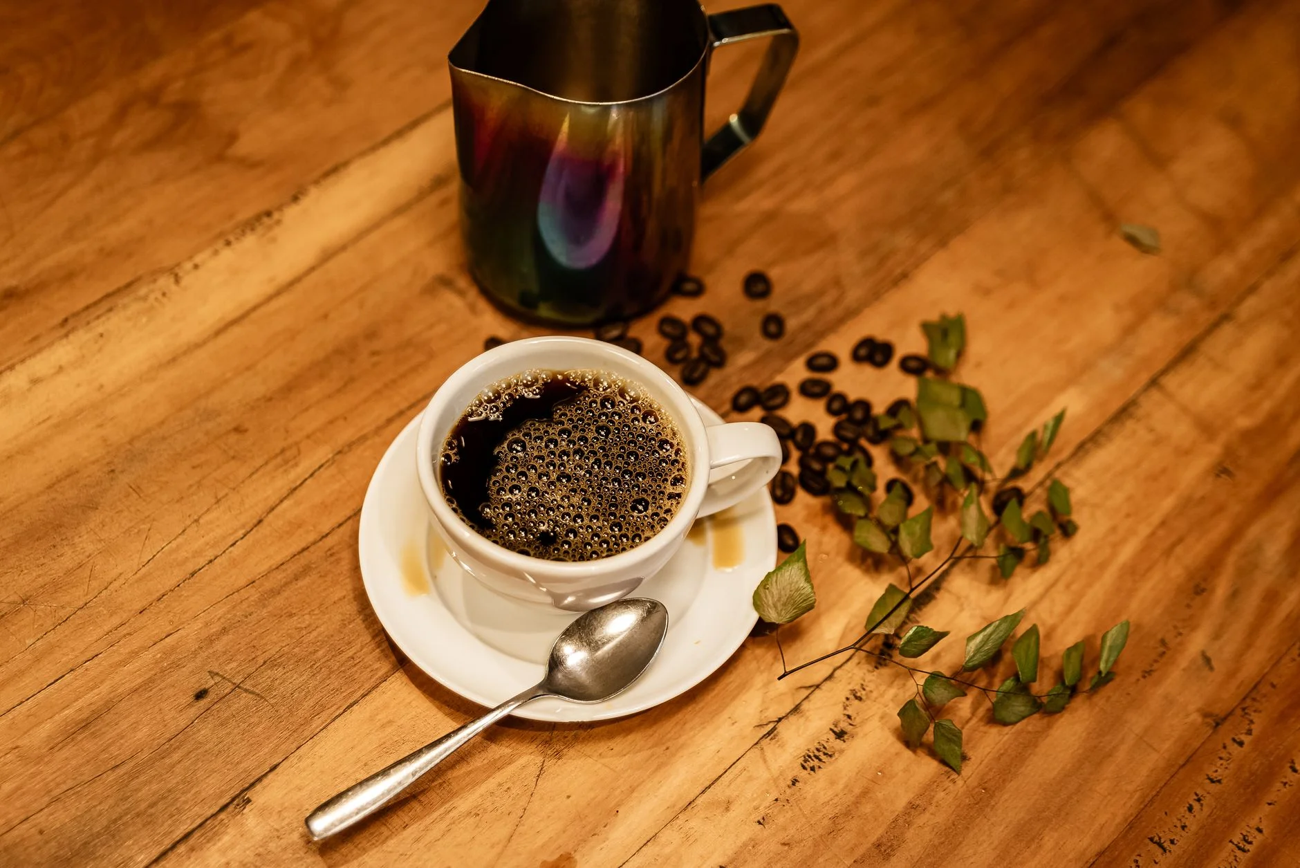 A photorealistic image of a vintage alarm clock showing 9:00 AM, with a steaming, artisan coffee cup placed next to it on a rustic wooden table. Sunlight streams through a window, creating soft shadows. Sharp focus on the clock and cup, depth of field blurring a cozy background. 8K hyper-detailed, cinematic lighting, shot on a high-end DSLR. Elegant coffee scene with a coffee cup, roasted beans, and a metal jug on a wooden table. — Foto: Vinícius Vieira ft / Pexels