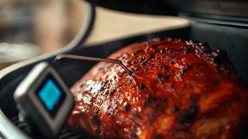 A close-up, photorealistic image of a digital meat thermometer probe inserted into a large, partially smoked piece of meat (e.g., pork shoulder or brisket) inside a professional smoker. The digital display shows a precise temperature reading. Cinematic lighting, sharp focus on the thermometer and meat, depth of field blurring the smoker interior, 8K, shot on a high-end DSLR.