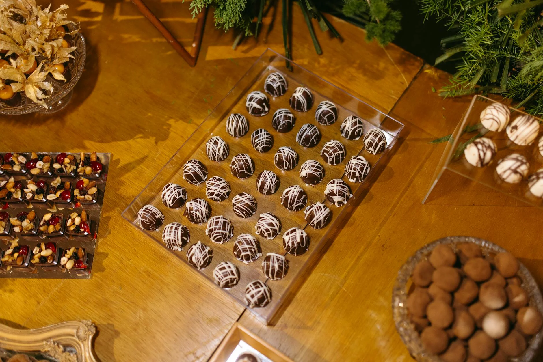 Photorealistic, professional photography, 8K, cinematic lighting, sharp focus, depth of field, shot on a high-end DSLR. A close-up of a perfectly tempered, glossy dark chocolate surface next to a piece of chocolate exhibiting 'fat bloom' with a dull, grayish film, highlighting the contrast in texture and appearance. In the background, scientific glassware or a food laboratory setting can be subtly blurred. A variety of gourmet chocolate truffles and nuts displayed on a wooden table. — Foto: Jonathan Borba / Pexels