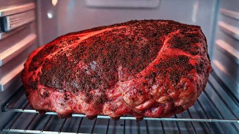 Photorealistic image of a large beef rib section generously coated with a dark, rich dry rub, resting on a metal rack inside a refrigerator. The meat should look plump and ready for smoking. Cinematic lighting, sharp focus, depth of field. 8K, professional photography. Photorealistic image of a large beef rib section generously coated with a dark, rich dry rub, resting on a metal rack inside a refrigerator. The meat should look plump and ready for smoking. Cinematic lighting, sharp focus, depth of field. 8K, professional photography.