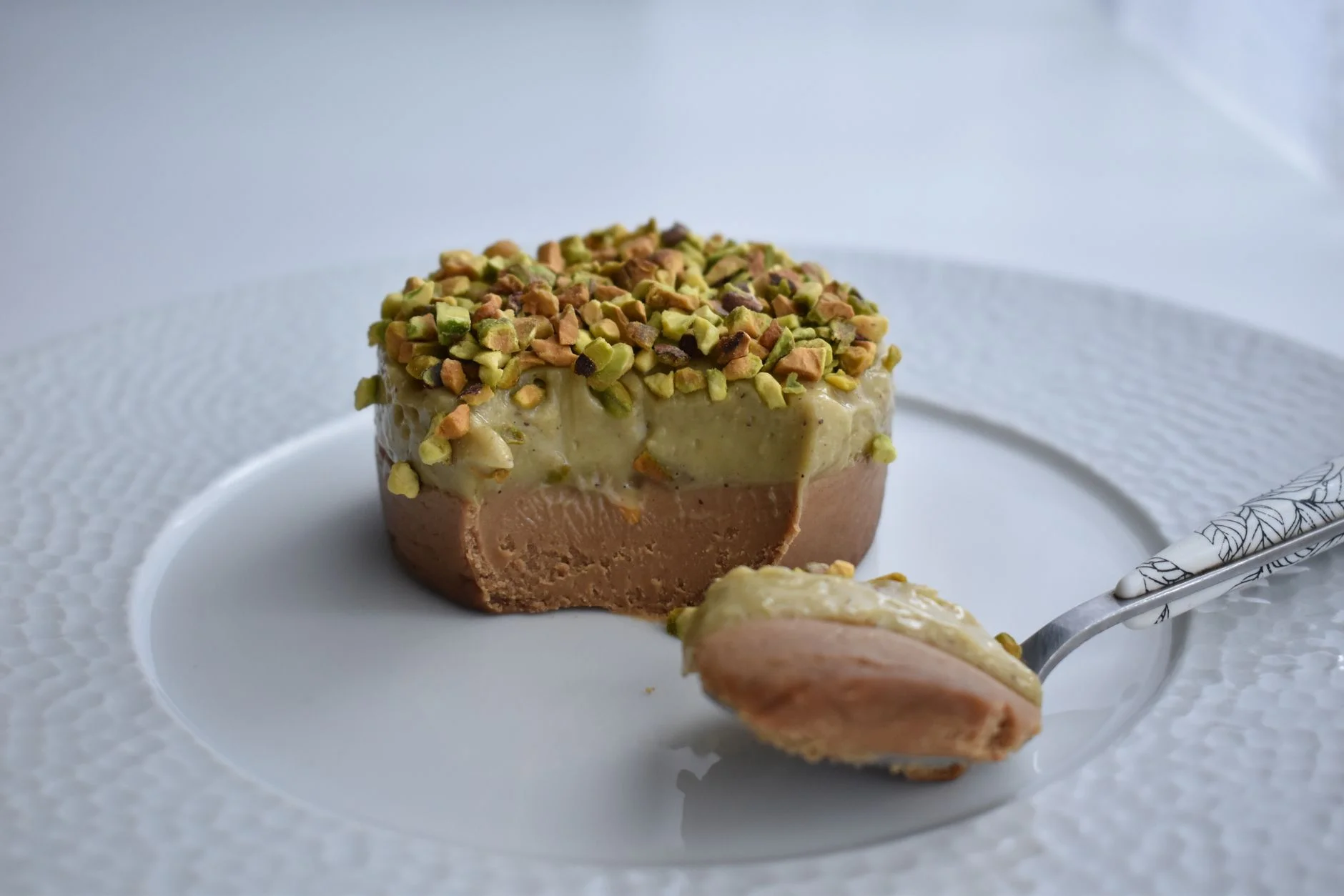 A photorealistic, professional photography, 8K, cinematic lighting, sharp focus, depth of field, shot on a high-end DSLR, of various vegan thickeners and fats laid out on a clean white marble surface: a bowl of refined coconut oil, a block of cocoa butter, a small bag of agar-agar powder, a container of cashew cream, and a small jar of xanthan gum. The lighting highlights their textures and forms, suggesting their functional diversity. Tasty mousse cake with chocolate cream and layer of greenery custard with chopped nuts on top placed on plate near silverware — Foto: tomateoignons / Pexels