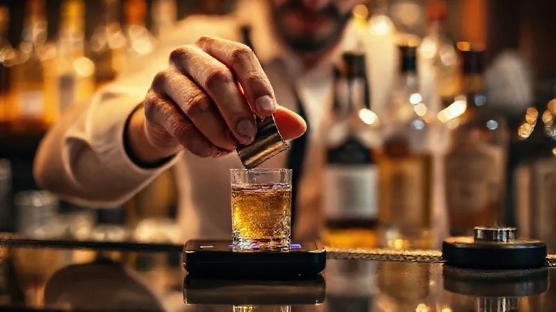 A photorealistic close-up of a bartender's hands meticulously measuring spirits with a high-quality jigger and a digital scale, bottles of various liqueurs blurred in the background. The scene is bathed in warm, cinematic lighting, emphasizing precision and craftsmanship. Sharp focus on the measuring tools and liquid, depth of field. Professional photography, 8K, shot on a high-end DSLR.