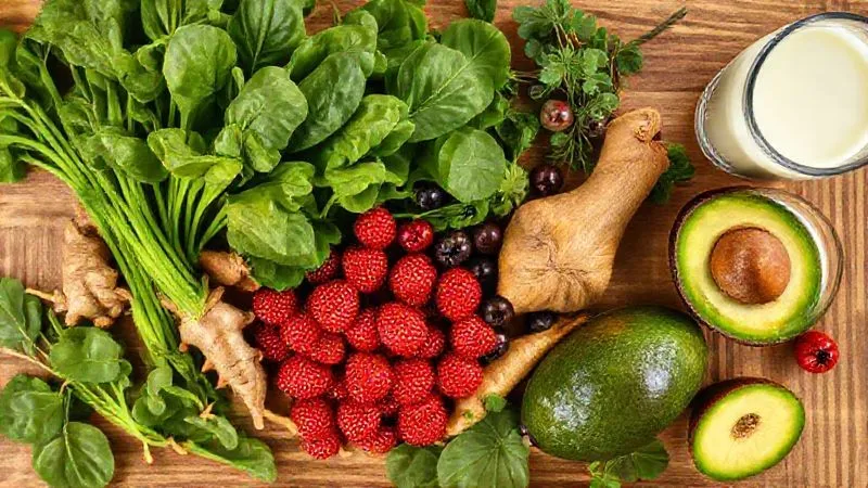 A photorealistic, professional photography overhead shot of a clean, wooden kitchen counter filled with colorful, fresh ingredients for a smoothie: vibrant green spinach, bright red berries, golden turmeric root, fresh ginger, a ripe avocado, and a glass of almond milk. All items are artfully arranged, with sharp focus, depth of field, 8K hyper-detailed, cinematic lighting, shot on a high-end DSLR, suggesting freshness and health.