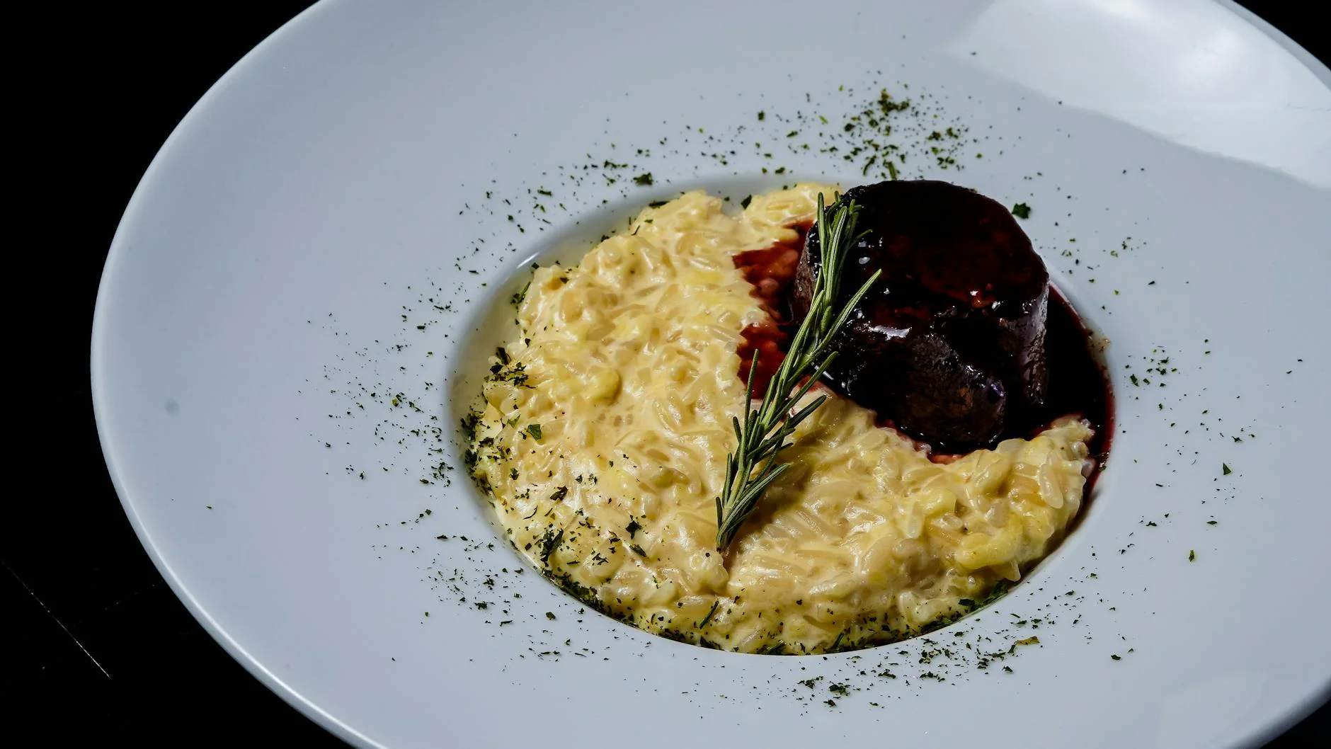 Delicious gourmet risotto with tender meat and rosemary sprig in a white plate. — Foto: pedro furtado / Pexels