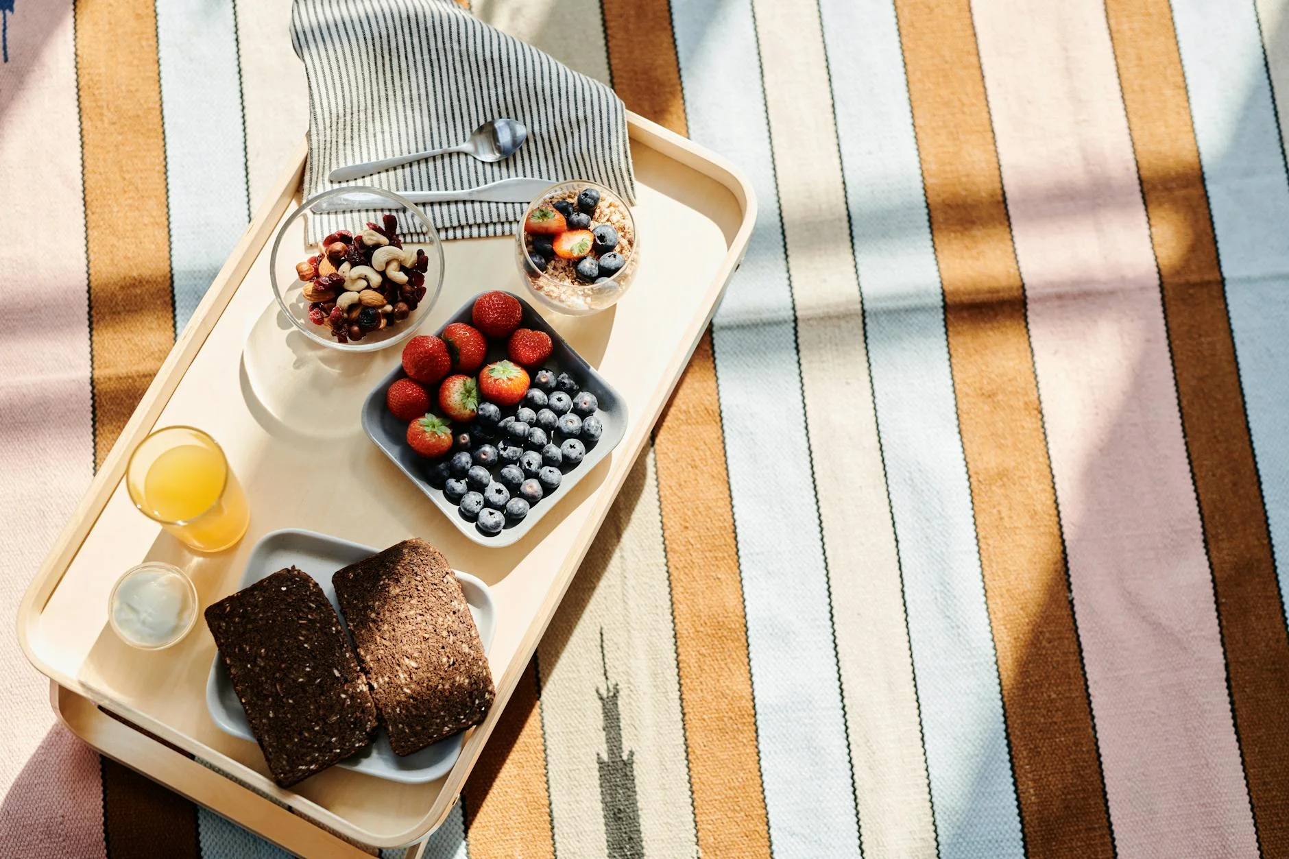 Top view of a healthy breakfast tray with fruits, bread, and juice on a striped tablecloth. — Foto: August de Richelieu / Pexels